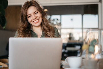 Image of young beautiful joyful woman smiling while working with laptop in office