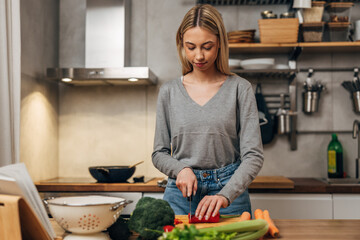 Front view of a young blonde woman is cutting vegetables