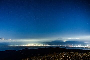 夜中の暗闇にぼんやりと浮かび上がる富士山と麓の市街地