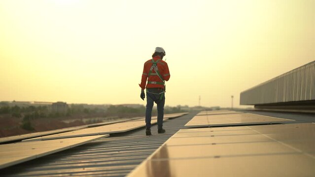 A technician sits on a rooftop, examining solar panels under a clear blue sky. He points while taking notes, ensuring everything is functioning properly.