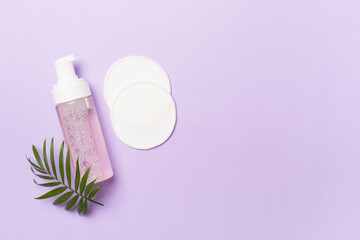 Foaming facial cleanser and with eco pads on color background, top view