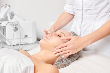 Cosmetologist rubbing moisturizing cream mask into woman face skin for rejuvenation, anti aging...