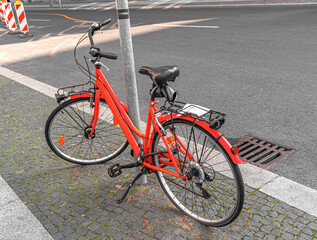 Fototapeta na wymiar A red bicycle is parked at a lamppost on a city street.