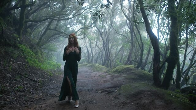 Beautiful woman in an elf costume is walking in a magic green enchanted forest.
