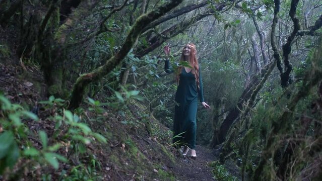 Beautiful woman in an elf costume is walking in a magic green enchanted forest.