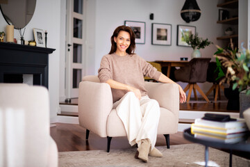 Attractive and smiling woman wearing casual clothes and relaxing in an armchair at home