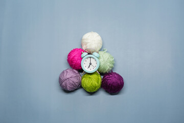 A small green alarm clock lies on woolen balls against a blue background. Time to knit.