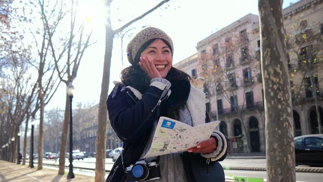 One young asian tourist woman looking for directions in a paper map visiting a european city on a weekend. Front view of a lady watching a location on a guide in a vacation trip. Travel concept. Slow