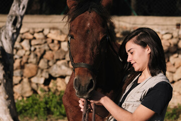 Brunette girl putting the reins on the horse's head.