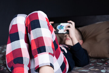 A teenage child is playing video games on the phone. Addiction to gadgets. A boy in pajamas.