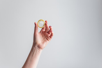 Una mujer sostiene un preservativo masculino sin envoltorio sobre fondo blanco. Sexo seguro....