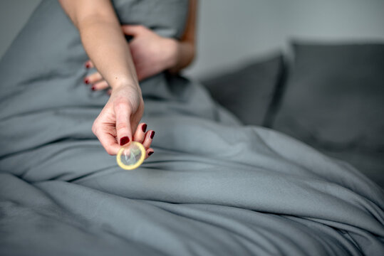 Detalle de una mujer en la cama sujetando un preservativo masculino sin envoltorio. Concepto de sexo seguro. Protecci&oacute;n contra embarazos y enfermedades de transmisi&oacute;n sexual.
