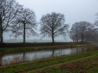 Wooden bench in fog alongside canal