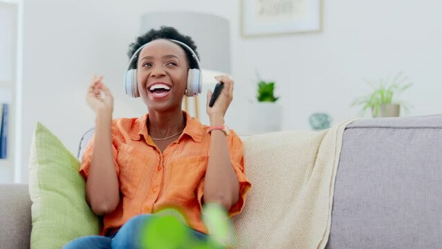 Woman dancing on couch with headphones, phone and music streaming for mental health, wellness and relaxing. African person dance on sofa and listening to audio technology on mobile app or cellphone