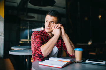 Thoughtful man sitting in cafe with coffee and copybook