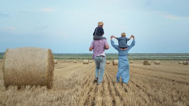 male children sit on shoulders of their parents while having fun in wheat field