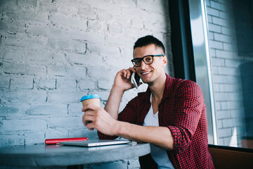 Cheerful young man talking on smartphone at cafe