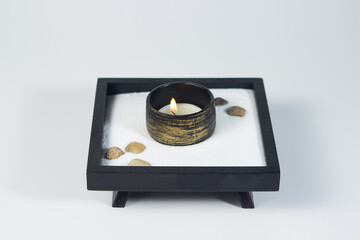 Burning tea candle on a wooden stand on a white background. little zen garden