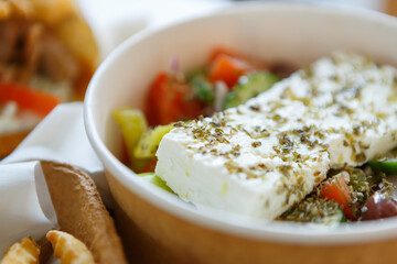 Traditional Greek salad with feta cheese, olive oil and fesh vegetables served in paper plate for take away