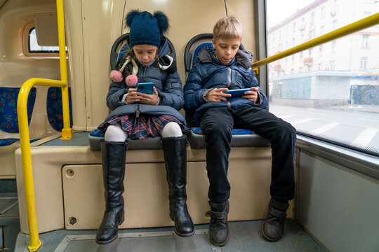 Children Are Watching Videos, Using Mobile Applications In Mobile Phones On City Bus. Internet Technology For Streaming Video On Mobile Phone In Public Transportation. Happy Caucasian Kids Uses Phones