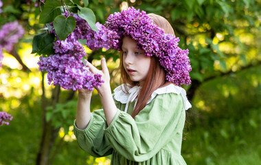 portrait of a girl with long red hair in a wreath of lilacs in the garden in spring
