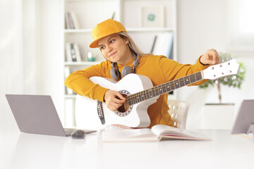 Young female learning to play an acoustic guitar in front of a laptop computer