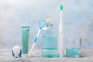 Electronic ultrasonic toothbrush, mouthwash, floss, tongue cleaner and toothpaste on blue textured...