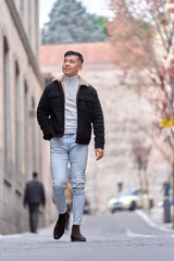 Asian man looking at camera and smiling while walking outdoors on the street.