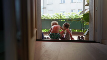 Children sitting by door step putting shoes on outside. Older brother helping younger sibling to...