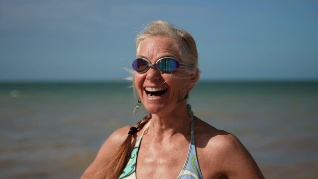 Extreme closeup portrait of laughing happy athletic pretty mature senior woman 50s, 60s, smiling wearing swim goggles at the beach to go swimming.
