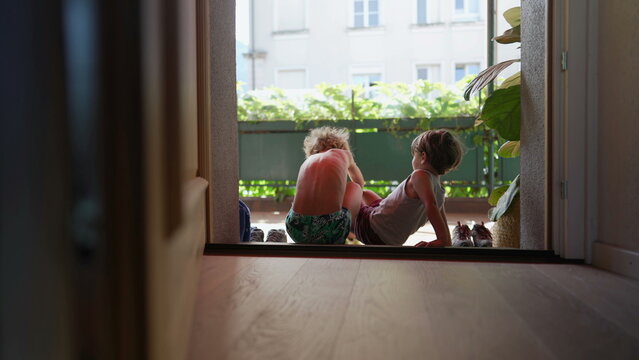 Children Sitting By Door Step Putting Shoes On Outside. Older Brother Helping Younger Sibling To Put Shoe By Doorstep