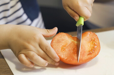 A little boy cuts a tomato with a knife.