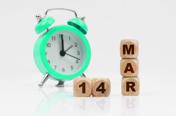 On a white background, a green alarm clock and a calendar with the inscription - March 14