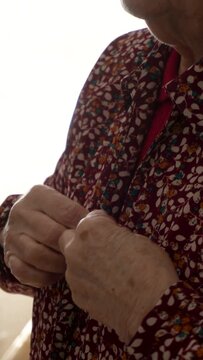 An older woman buttons up a spring-patterned shirt.