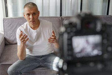 Confident successful man talking and recording vlog on camera in home interior.