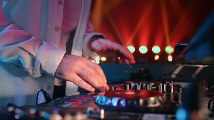 DJ male hands mixing music regulating turntable console controlling CD illuminated nightclub party