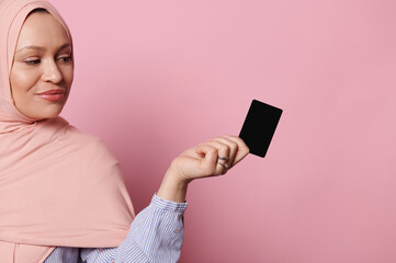Confident attractive Arab Muslim woman with head covered in pink hijab, holding a black plastic...