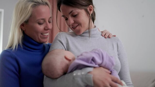 Authentic gay lesbian couple of mothers and newborn baby having tender moment at home - Lgbt family concept