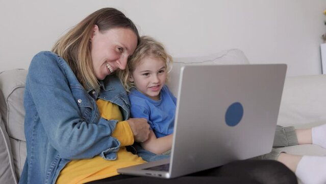 Happy mother and kid son watching videos having fun in computer laptop at home living room