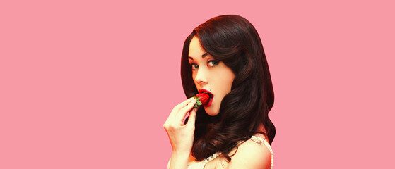 Portrait of attractive brunette sexy woman enjoying taste of fresh strawberry on pink background