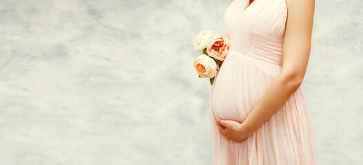Portrait of beautiful young pregnant woman with bouquet of flowers on background