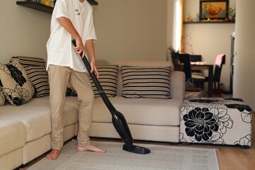The guy, a teenager of thirteen, cleans the house, vacuums the floor, the sofa, the boy cleans up...