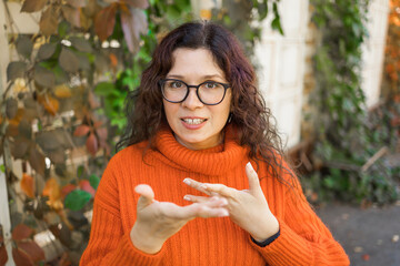 Happy curly woman blogger smiling face talking to webcam recording vlog. Social media influencer...