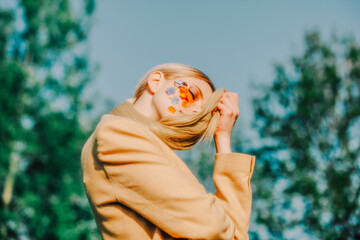 Blonde girl in brown jacket with flowers on face at outdoor