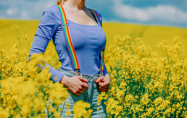Beautiful female in rainbow LGBT suspenders for pants in rapeseed field