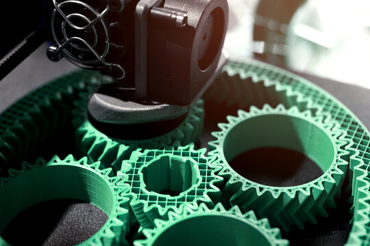 Detail view on print head of 3D-printer making a planetary gear part from mint coloured plastic. selective focus. Visible infill structure and layers at printed part. Modern production concept