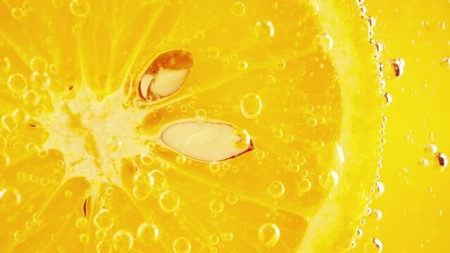 A slice of ripe orange in water bubbles on an orange background.