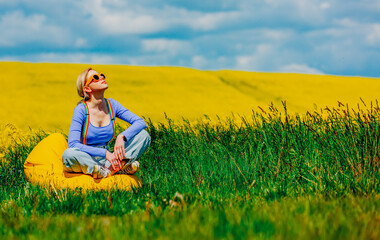 Beautiful female in rainbow LGBT suspenders for pants sitting in bean chair in rapeseed field