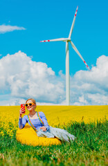Beautiful female in rainbow LGBT suspenders for pants and mobile phone is sitting in bean chair in rapeseed field