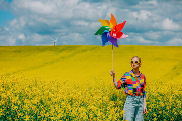 Beautiful female in 90s stylish shirt with pinwheel in rapeseed field